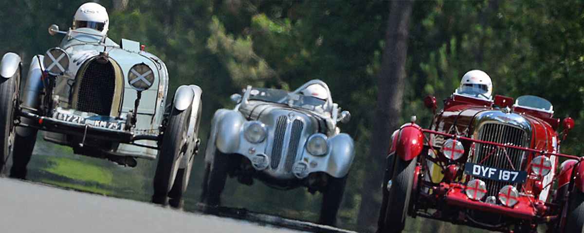 Three classic racing cars driving around the Le Mans circuit